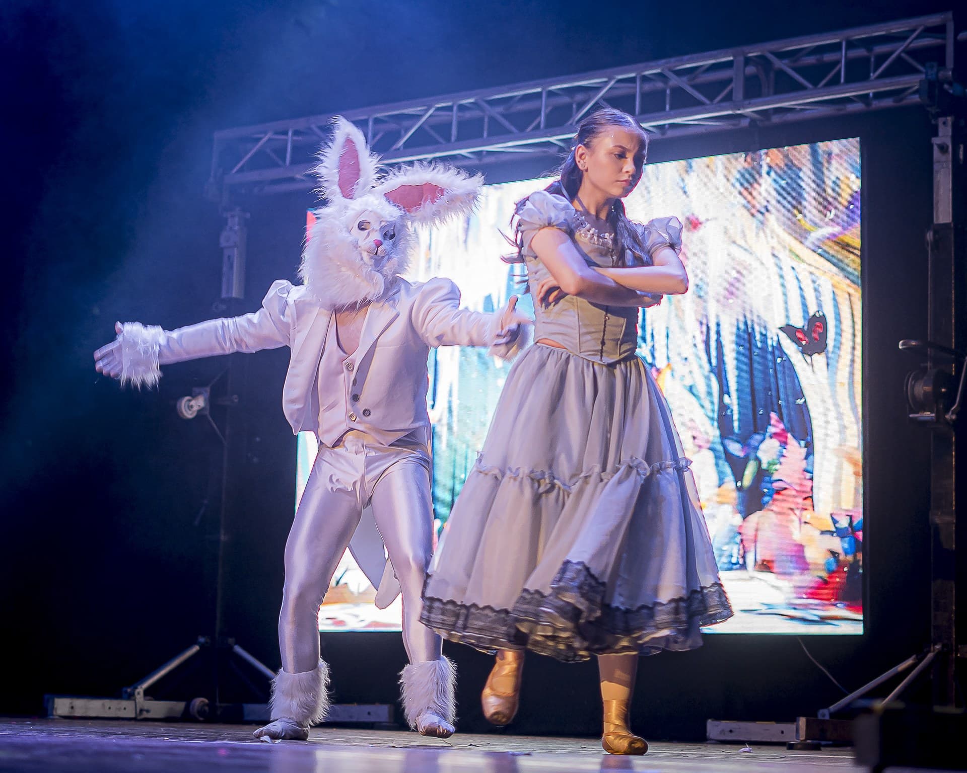 El Conejo Blanco y Alicia bailando en escena frente a una pantalla LED