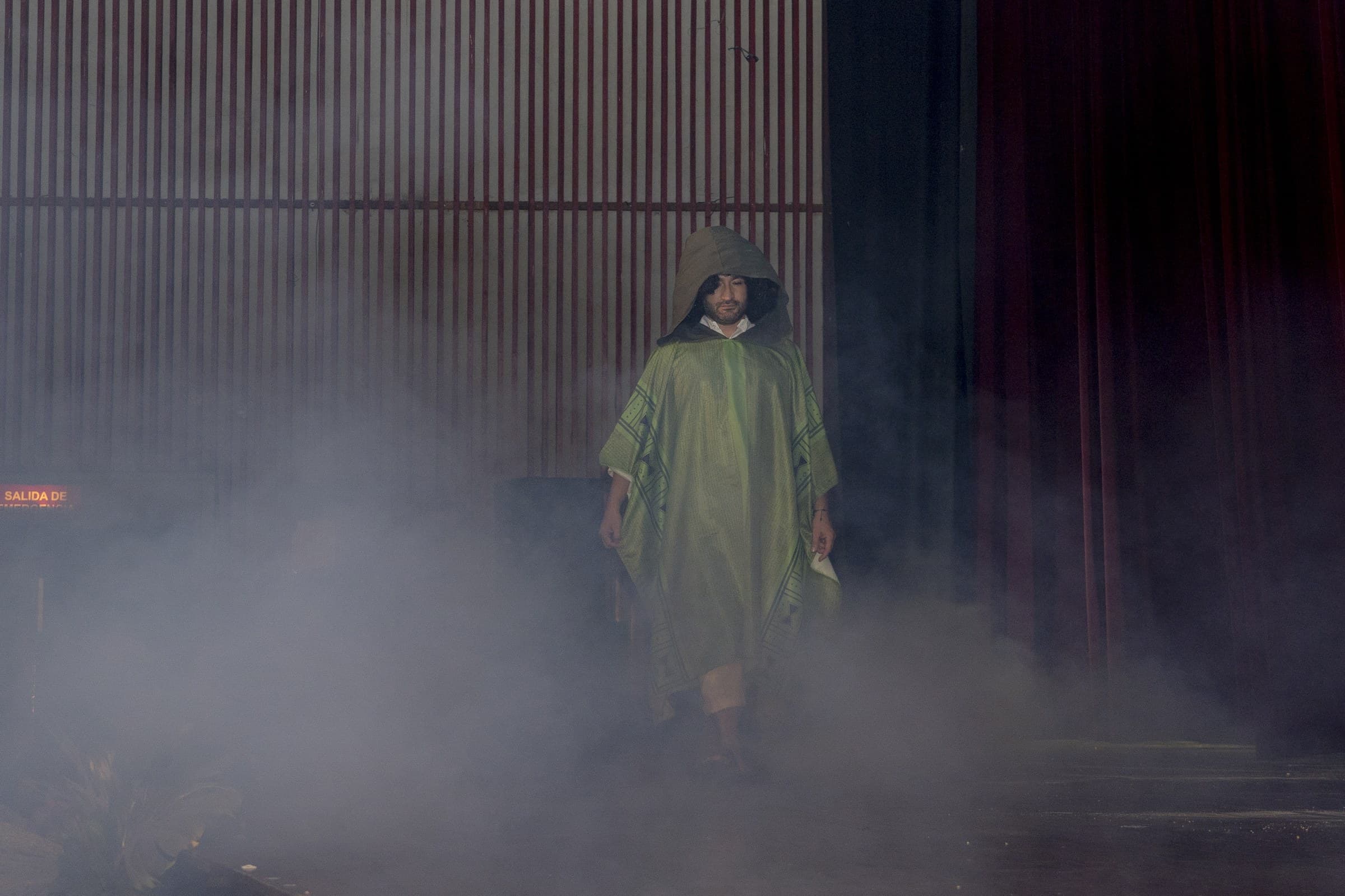 Bailarín con poncho verde entre la niebla del escenario